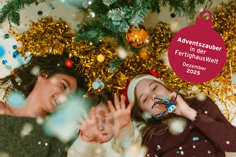 Familie liegt lachend unter dem Weihnachtsbaum mit Konfetti und Deko, feiert Adventszauber in der FertighausWelt im Dezember 2025.