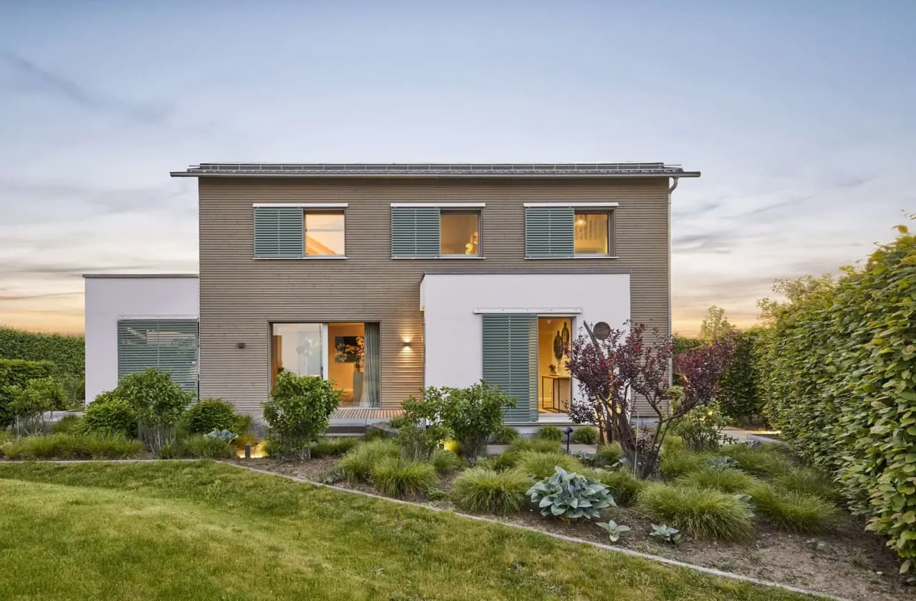 Modernes Plusenergiehaus mit klarer Architektur, nachhaltiger Holzfassade, großen Fenstern und energieeffizientem Design, umgeben von gepflegtem Garten bei Sonnenuntergang