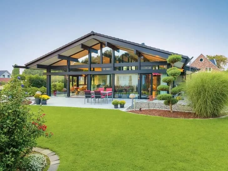Modernes Einfamilienhaus mit großer Glasfront und gepflegtem Garten mit Rasen und Zierpflanzen an sonnigem Tag
